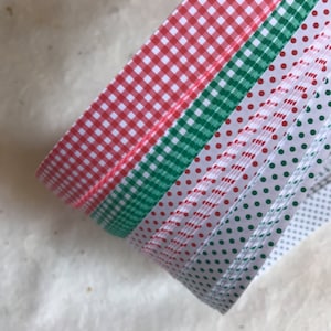 May include: A roll of red and green patterned washi tape. The tape has a gingham pattern, a polka dot pattern, and a striped pattern.