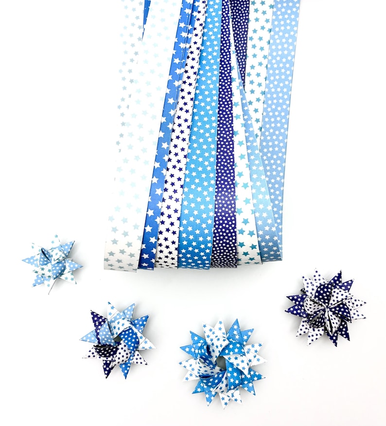 May include: An assortment of blue and white patterned paper ribbons and star-shaped paper ornaments. The ribbons feature various shades of blue with white star patterns. The ornaments are made from folded paper in coordinating colors and patterns.