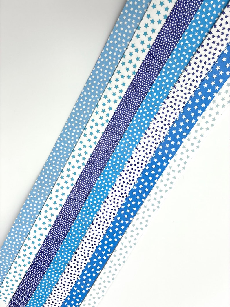 May include: An assortment of blue and white patterned ribbons with star designs. The ribbons vary in shades of blue, from light to dark, and feature different star patterns, including small dots and larger stars.