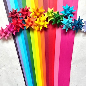 May include: A collection of multi-colored paper strips arranged in a fan shape, featuring a spectrum of colors including purple, blue, green, yellow, orange, red, and pink, topped with several folded three-dimensional paper stars.