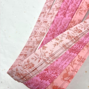 May include: Close-up of several pink floral patterned ribbons in varying shades. The ribbons are arranged diagonally, showcasing a detailed design of flowers and leaves. The color palette includes light and dark pink tones.