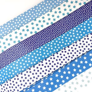 May include: An assortment of blue paper strips, each adorned with a pattern of white stars. The shades of blue vary from light to dark, creating a gradient effect. The strips are arranged diagonally, offering a visually appealing design.