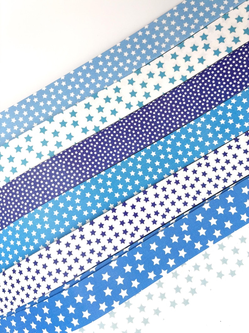 May include: An assortment of blue paper strips, each adorned with a pattern of white stars. The shades of blue vary from light to dark, creating a gradient effect. The strips are arranged diagonally, offering a visually appealing design.