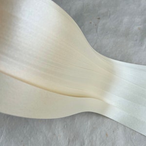 May include: A close-up of a roll of white, thin, paper-like material. The material is folded in half and the edges are visible.