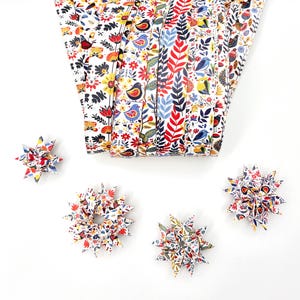 May include: A collection of colorful origami stars and folded fabric with a floral and bird pattern. The fabric is white with red, blue, yellow, and green flowers and birds. The origami stars are also patterned with the same design.