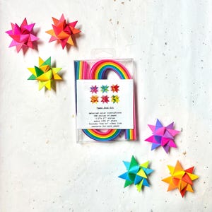 May include: A Paper Star Kit with detailed instructions, rainbow-colored paper strips, and six colorful origami stars. The kit includes 100 strips of paper, each 1/2" x 17", to make 25 stars. The stars are in shades of pink, orange, yellow, green, and blue.