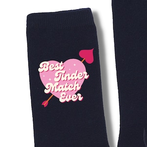 May include: A pair of navy blue socks with a pink heart graphic that says "Best Tinder Match Ever".