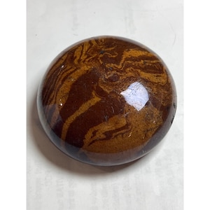 May include: A polished, round stone with a swirling pattern of dark brown and tan colors. The stone has a smooth, glossy surface and a natural, earthy appearance. The stone is a decorative item.