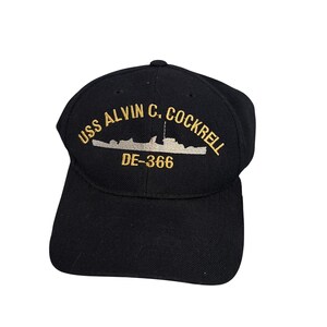 May include: Black baseball cap with the text "USS ALVIN C. COCKRELL DE-366" embroidered in gold. The cap features a curved brim and a structured crown, suitable for outdoor wear.