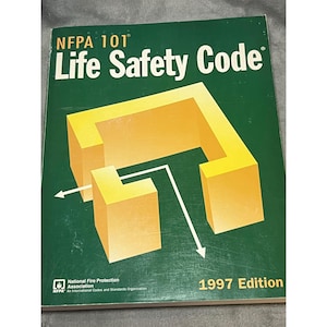 May include: A green book titled "NFPA 101 Life Safety Code" with a yellow geometric design and white arrows. The book is the 1997 Edition and is published by the National Fire Protection Association.