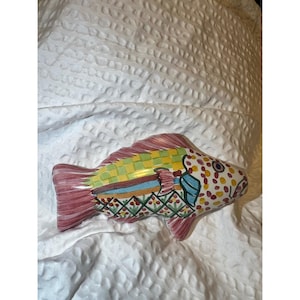 May include: A ceramic fish figurine with a colorful design. The fish has a red tail and fins, a yellow and green checkered pattern on its back, and a dotted pattern on its body. The fish has a blue accent and a detailed design.