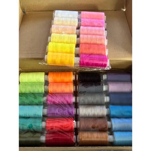 May include: A collection of colorful spools of thread, neatly arranged in a cardboard box. The threads are in a variety of colors, including white, yellow, pink, orange, green, blue, purple, black, gray, and brown. The spools are tightly wound and ready for use.