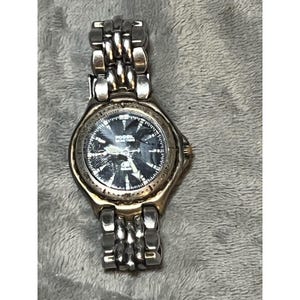 May include: A Fossil watch with a silver-tone metal band and a black watch face. The watch face has white markings and the brand name "Fossil" is visible. The watch has a gold-tone bezel.