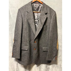 May include: A gray tweed blazer with brown elbow patches and brown buttons. The blazer is hanging on a wooden hanger. The interior lining is a dark gray color.