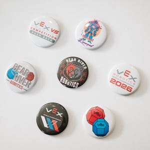 Puede incluir: Una colección de botones redondos para competiciones de robótica VEX. Los botones son blancos y negros, con texto y gráficos, incluyendo "VEX V5 COMPETITION PUSH BACK", "Bear River Robotics" y "VEX Robotics 2026".