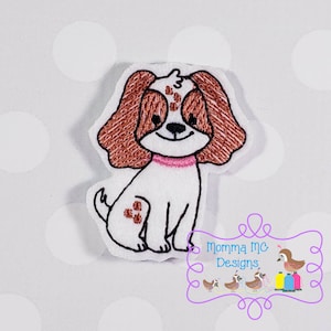 May include: Embroidered felt applique of a brown and white dog with pink collar. The dog is sitting with its tail curled behind it.