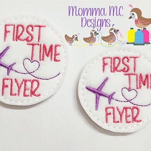 May include: Two circular white fabric patches featuring pink embroidered text that reads FIRST TIME FLYER. Each patch includes a purple airplane icon with a stitched flight path forming a heart shape. The edges are finished with white stitching.