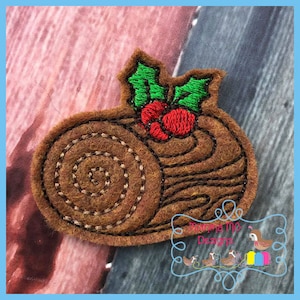 May include: Embroidered felt yule log with green holly leaves and red berries. The log is brown and has a swirl pattern.