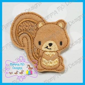 May include: A brown felt squirrel applique with embroidered details. The squirrel has a fluffy tail and a smiling face. The design includes the text "Momma MC Designs" in a decorative frame. This applique is suitable for crafting projects.