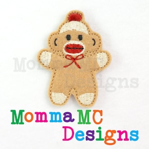 Può includere: Applicazione a forma di omino pan di zenzero in feltro marrone, con papillon rosso e cappello rosso e bianco. L'applicazione ha una faccia da scimmia calzino con labbra rosse e un contorno cucito bianco e marrone. Il testo "Momma MC Designs" è sotto.