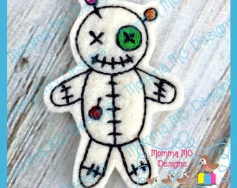 May include: White felt voodoo doll with black stitching, a red button, and a green eye. The doll has a stitched-on smile and a single pin with colorful beads on top of its head.