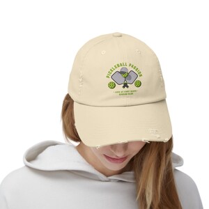 Könnte beinhalten: Eine beige, abgenutzte Baseballkappe mit einem grün-weißen Pickleball-Logo und dem Text "Pickleball Passion - Love at First Serve - Pickleball Club".
