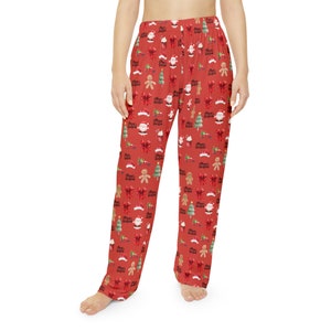 Op de afbeelding: Rode pyjamabroek met een feestelijk kerstpatroon. Het ontwerp bevat de kerstman, peperkoekenmannen, kerstbomen, strikken en de tekst "Merry Christmas". De broek is gemaakt van een zacht, comfortabel materiaal.
