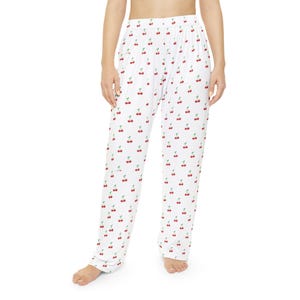 May include: White pajama pants with a repeating pattern of red cherries and green stems. The pants are made of a soft, lightweight fabric and have a relaxed fit. The pajama pants are suitable for lounging or sleeping.