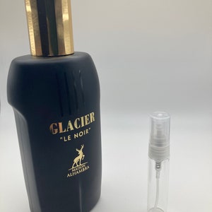 May include: A black glass bottle of Glacier "Le Noir" perfume by Maison Alhambra. The bottle has a gold cap and a gold deer logo on the front. A small clear glass sample bottle with a white spray nozzle is also shown.