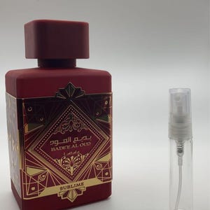 May include: A red bottle of perfume with a gold label that says "Badr Al Oud" and "Sublime". The bottle is next to a small clear glass bottle with a spray nozzle.