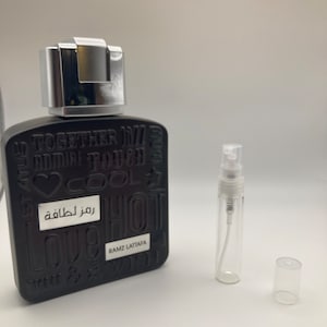 May include: A black rectangular bottle of perfume with a silver cap. The bottle has white text that says "Together in 7", "Cool", "Love Hot", "You & Me", and "Ramz Lattafa". There is a white label with the Arabic text "رمز لطافة". The bottle is next to a clear glass sample vial with a silver cap and a clear plastic cap.