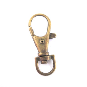 May include: A gold-toned metal swivel clasp hook. The hook is closed and ready to be attached to a keychain, bag, or other item.