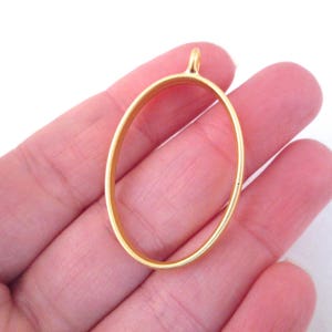 May include: Gold oval pendant bezel setting for jewelry making. The bezel is a smooth, shiny metal with a loop at the top for attaching a chain or cord.