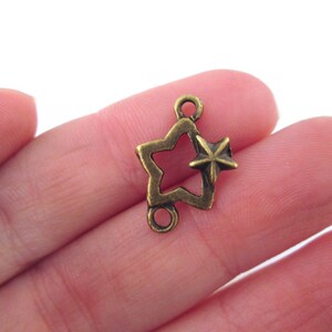 May include: A gold-toned metal star charm with a smaller star cutout in the center. The charm has two loops for attaching to jewelry or other crafts.