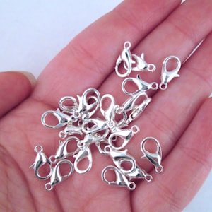 May include: A close-up of a pile of silver-toned lobster claw clasps. The clasps are small and delicate, and they are perfect for adding a touch of elegance to jewelry.