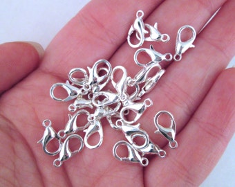 May include: A close-up of a pile of silver-toned lobster claw clasps. The clasps are small and delicate, and they are perfect for adding a touch of elegance to jewelry.