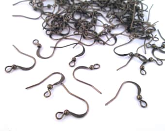 May include: A pile of bronze-colored earring hooks, scattered on a white surface. The hooks are made of metal and have a small ball at the top.