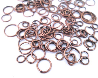 May include: A large assortment of copper jump rings in various sizes. The jump rings are scattered on a white surface.