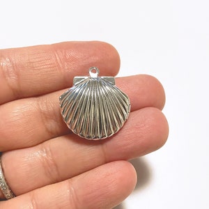 Może przedstawiać: Srebrny zawieszka w kształcie muszli z detalicznym, żebrowanym wzorem. Zawieszka ma pętelkę u góry do przymocowania do biżuterii lub innych prac rękodzielniczych.