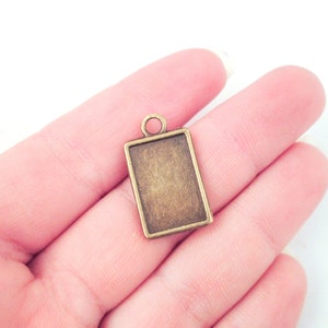 May include: A small, rectangular, bronze-colored pendant with a loop at the top. The pendant is blank and ready to be customized.
