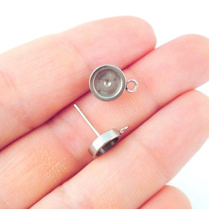 May include: Two silver-toned earring settings with a round bezel and a loop for attaching a finding. The settings are designed to hold a cabochon stone.