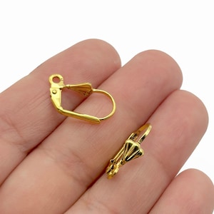 Op de afbeelding: Twee gouden oorclips met een decoratief ontwerp. De clips zijn gemaakt van metaal en hebben een veermechanisme.