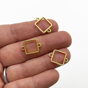 May include: Three gold-toned metal square frames with open sides and two jump rings on each side. The frames are different sizes.