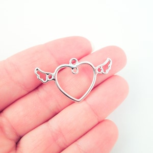 May include: Silver metal heart charm with wings. The heart is open and has a loop at the top for attaching to a necklace or bracelet.