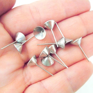 May include: A close-up of a pile of silver earring posts with cone-shaped tops. The posts are designed to hold a variety of charms or beads.