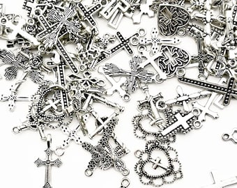 May include: A collection of silver-colored cross charms in various designs, including ornate, simple, and heart-shaped crosses. The charms are scattered on a white surface, showcasing their intricate details and textures. Ideal for jewelry making or craft projects.