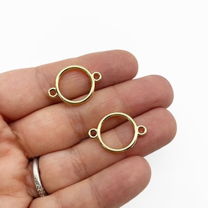 以下が含まれることがあります： 2つの金色の金属製の円形コネクタ。それぞれに2つのジャンプリングが付いています。コネクタの直径は約2.5cmです。
