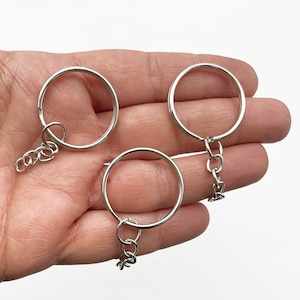 May include: Three silver key rings with attached chains. The key rings are circular and the chains are made of small, linked metal pieces.