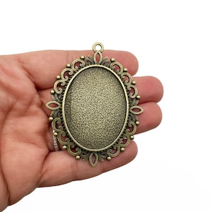 May include: An antique gold oval pendant with a decorative filigree design. The pendant is blank and ready to be customized with a design or image.