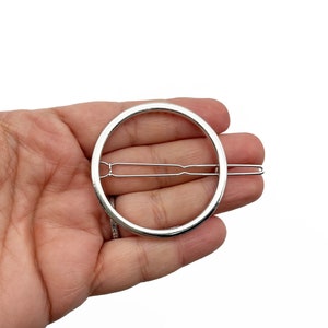May include: A silver-colored hair barrette with a circular design. The barrette features a simple, elegant circle with a metal clasp for securing it in the hair. The barrette is shown against a white background.
